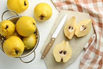 Naklejka na ściany i meble Tasty ripe quinces, metal colander and knife on white wooden table, flat lay