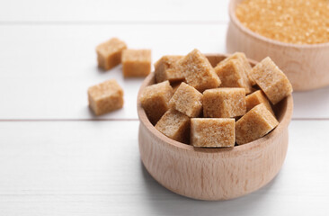 Brown sugar cubes in bowl on white wooden table, closeup. Space for text