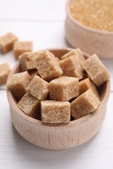 Brown sugar cubes in bowl on white table, closeup