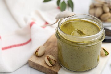 Tasty pistachio cream in jar and nuts on table, closeup. Space for text