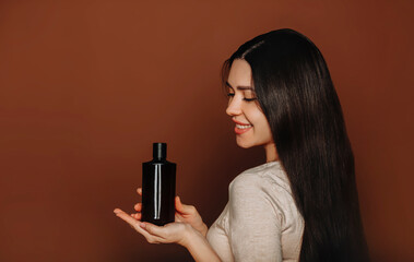 Young smiling woman with long healthy brown hair holding shampoo on palm, with organic, natural...