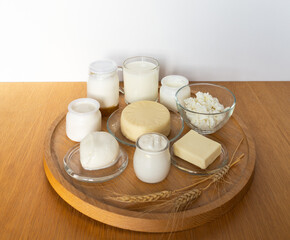 Delicious fresh organic dairy products - milk, cottage cheese, butter, cheese, yogurt, sour cream, mozzarella on wooden table and wheat ears on round tray