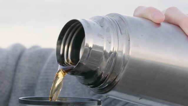 Pouring a hot drink from a thermos into a mug against the backdrop of the sea. Hot tea in a thermos. Slow motion. Hot tea
