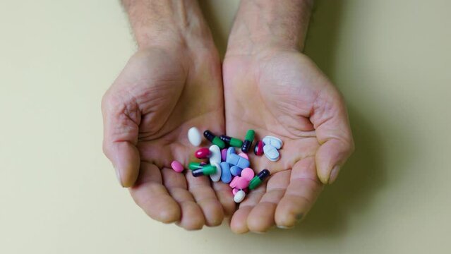 Unrecognizable senile hands white background, in which large number of different tablets are poured.