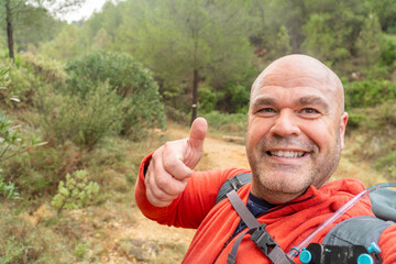 Smiling hiker takes a photo selfie doing thumbs up.