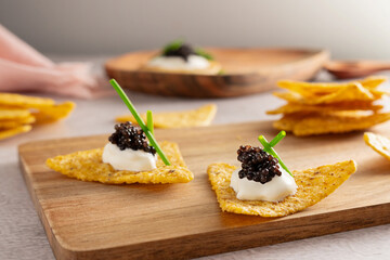Black caviar on nachos with sour cream on a wooden cutting board.
