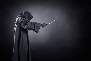 Wizard with hooded cape and magic wand over dark misty background