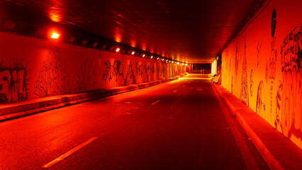 Circulation d'un tunnel urbain, avec des coureurs, complètement éclairé par des lumières rouges intense, circulation libre, ambiance mystérieuse, sombre, zone industrielle, la nuit, ciel nuit noir, 