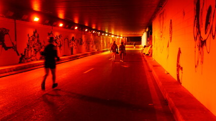 Circulation d'un tunnel urbain, avec des coureurs, complètement éclairé par des lumières rouges...