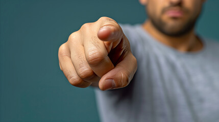 Close-up of man pointing finger directly at camera on teal background