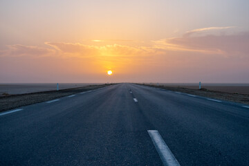 Beautiful colourful sunset over endless empty road in middle of desert. Asphalt highway in Tunisia, North Africa.