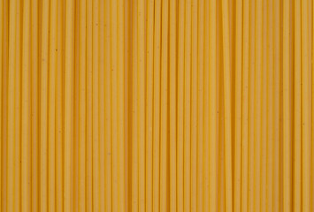 Parallel lines of uncooked spaghetti create a linear pattern on a yellow background, perfect for...