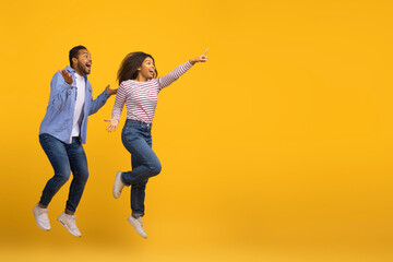 Fototapeta na wymiar Cool Offer. Excited Joyful Black Couple Jumping And Pointing At Copy Space