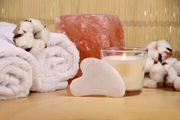 Gua sha facial stone, salt lamp, towels and candle on wooden background still life stock photo images. Spa and wellness setting with massage stone. Beauty spa treatment composition images