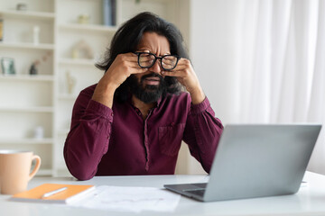 Tired indian man rubbing eyes, suffering from eyestrain during working on laptop