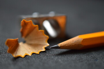 close up of pencil shavings, pencil sharpener and pencil on dark gray 