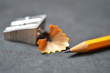 close up of pencil shavings, pencil sharpener and orange pencil on dark gray 