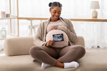 Happy black pregnant woman sitting on couch with baby sonography - obrazy, fototapety, plakaty
