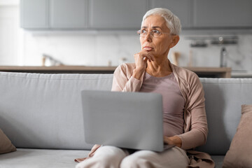 Worried senior woman using laptop computer in modern living room