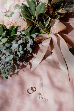 Flat lay of a coquette wedding bouquet with pink bow made from ribbons. Rings and wedding details. 