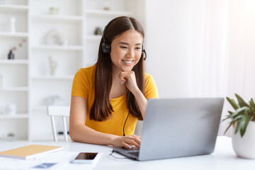 Focused asian woman wearing headset working on her laptop in home office