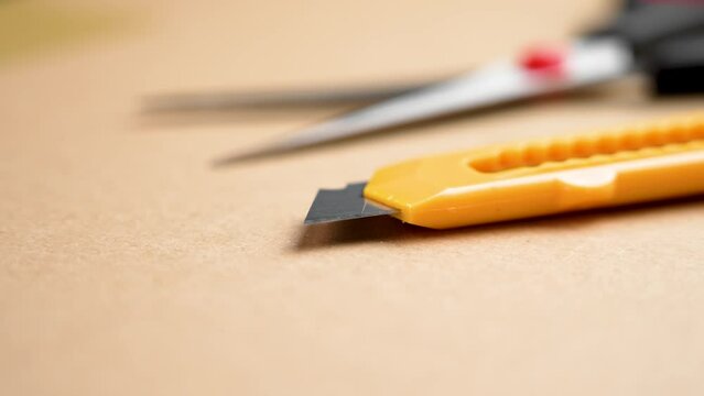 Stationery knife and sharp scissor on brown parcel box cardboard. Office stationery close up. Rotation