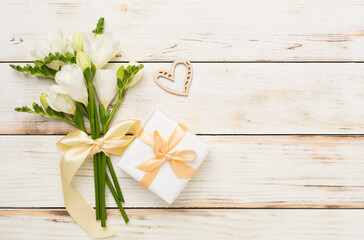 Gift box with freesia flower on wooden background, top view