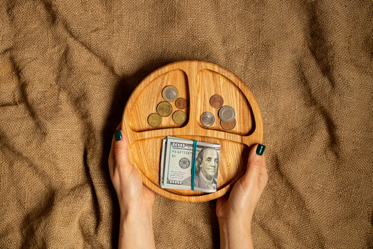 Female hands hold a wooden portion plate with dollars and coins on a background of brown fabric, business