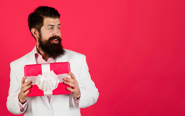 Bearded man in white suit with present box look aside on copy space for advertising. Birthday or anniversary. Smiling businessman in formal wear with gift box. Season sale. Discount. Shopping concept.