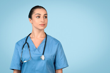 Portrait of european lady nurse posing and looking at free space isolated over blue studio background
