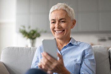 Portrait of happy mature lady surfing internet communicating on cellphone