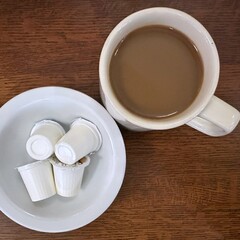 A cup of coffee with cream in a white mug next to a bowl of packaged coffee creamers