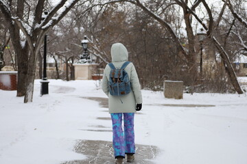 Warmly dressed for the harsh Canadian weather, a girl in ski pants and a warm jacket against the background of a winter park in Regina. © Uliana