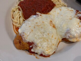 Melted mozzarella cheese on chicken parmesan with a side of spaghetti with sauce