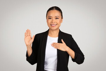 Professional Asian businesswoman making a pledge or oath gesture with a raised right hand - obrazy, fototapety, plakaty