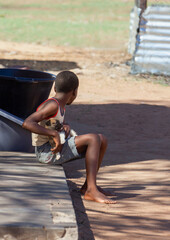 african child holding a puppy resting in the yard sitting in the shade