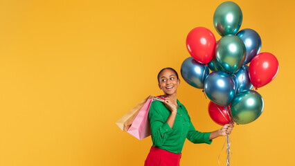 Fototapeta na wymiar Joyful black teen girl with shopping bags and balloons, studio