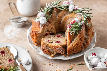 Christmas bundt cake decorated with glaze, cranberries and rosemary served on beige table. Homemade cake recipe