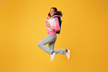Fototapeta na wymiar Smiling african american youngster girl jumping with her backpack, studio
