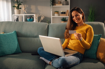 Woman at home holding credit card and using a laptop for an online shopping