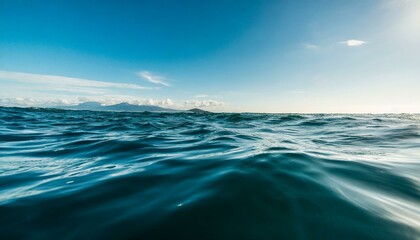 Obraz premium Ocean waves with sun, sky, and clouds in the background