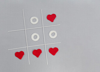 A tic tac toe game lies on a gray or silver background. Crochet elements, white zeros and red...