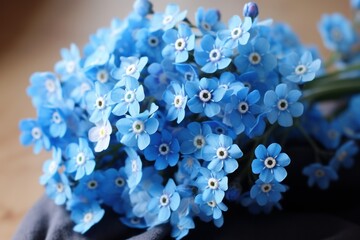  a bunch of blue flowers sitting on top of a piece of cloth next to a pair of gloves on a table. - obrazy, fototapety, plakaty