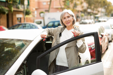 Mature lady standing beside her car with keys in hand and looking in camera.