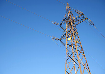 An electric pylon with blue sky in the background and rust on the supporting structure