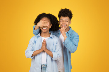 Two cheerful young people share a playful moment, with one covering the other's eyes
