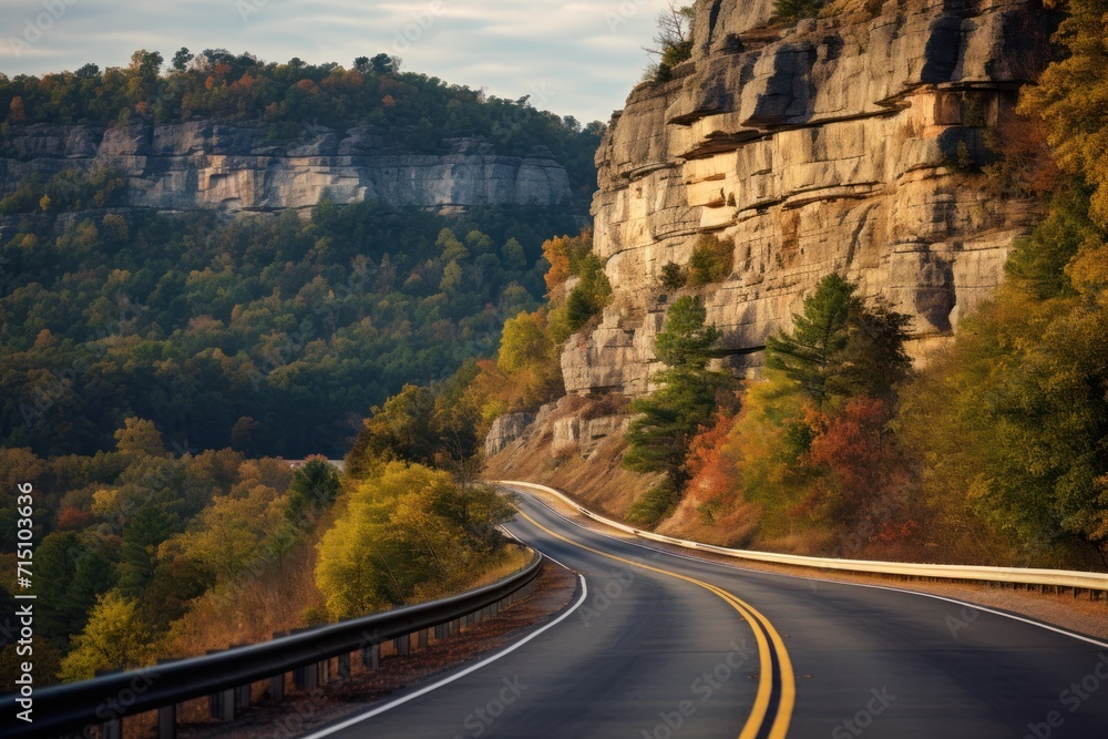 Poster a curve in the road in front of a mountain with trees on both sides and a cliff on the other side.