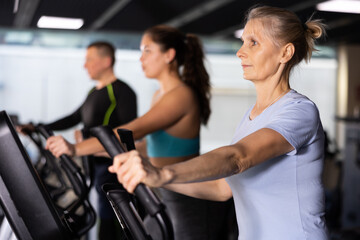 Focused mature woman using elliptical machine in gym