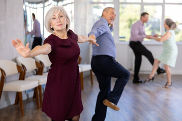Beautiful mature woman in modern dance salon studying with her partner to dance couples ballroom...