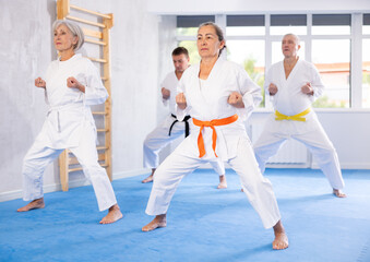 Active mature woman wearing kimono training karate techniques in group during workout session